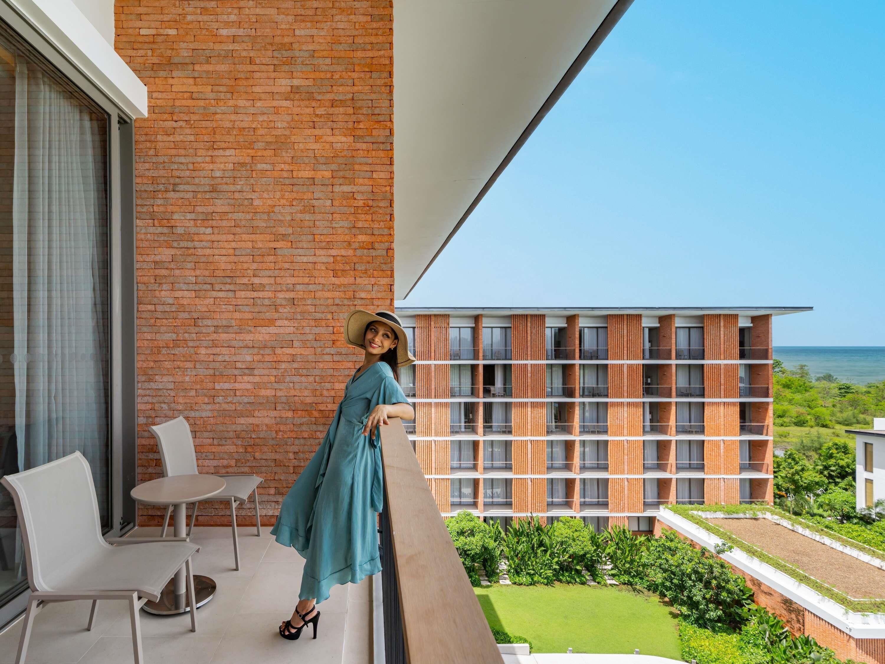 Un balcón con vista al mar, una pared de ladrillo y un edificio moderno con balcones.