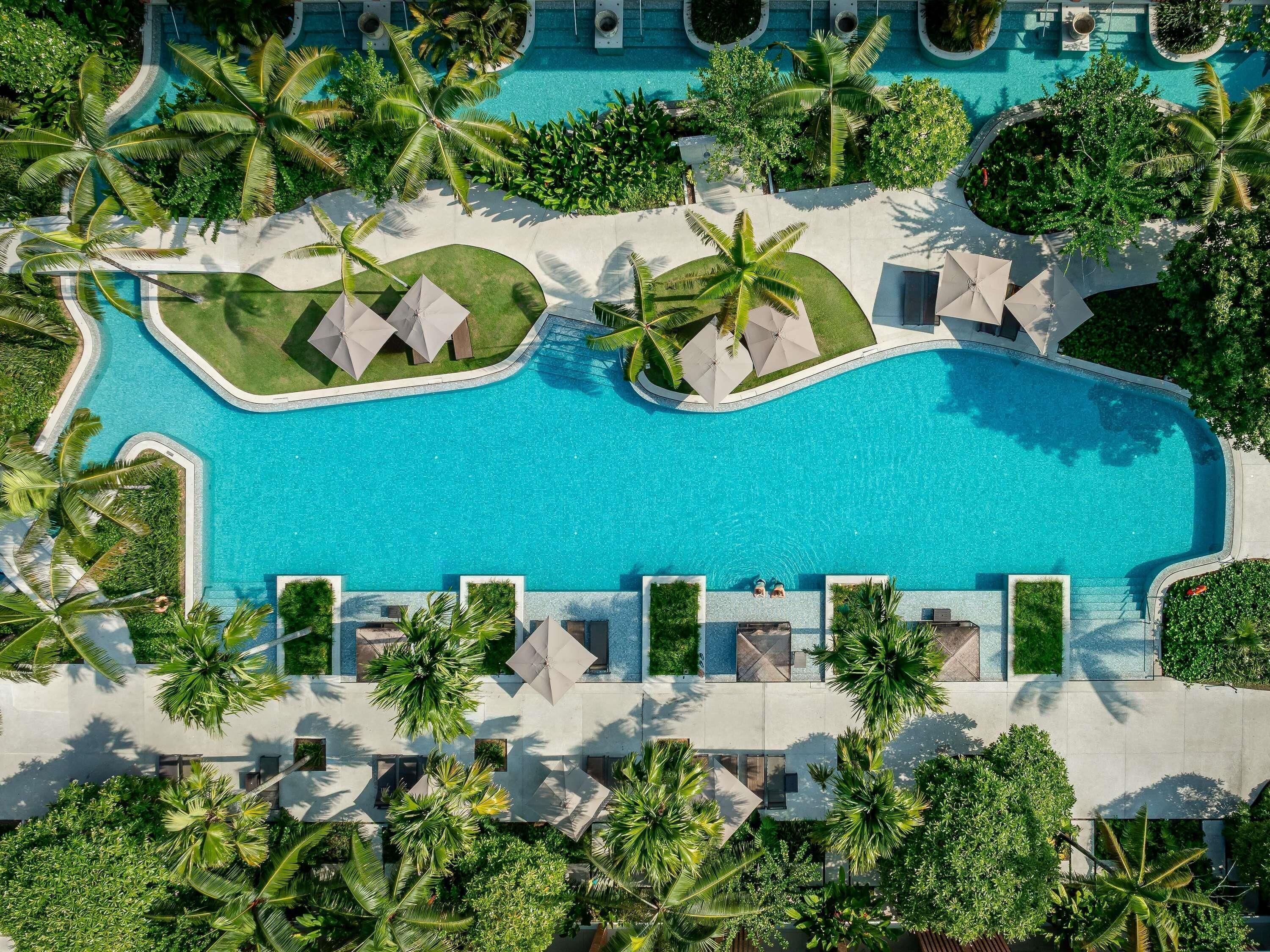 Vista aérea de un resort con piscina central rodeada de palmeras y zonas de descanso.