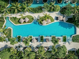 An aerial view of a resort with a central swimming pool surrounded by palm trees and lounge areas.