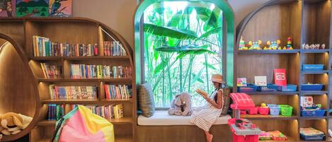A cozy reading nook with a large window, a bookshelf, and a toy kitchen set.