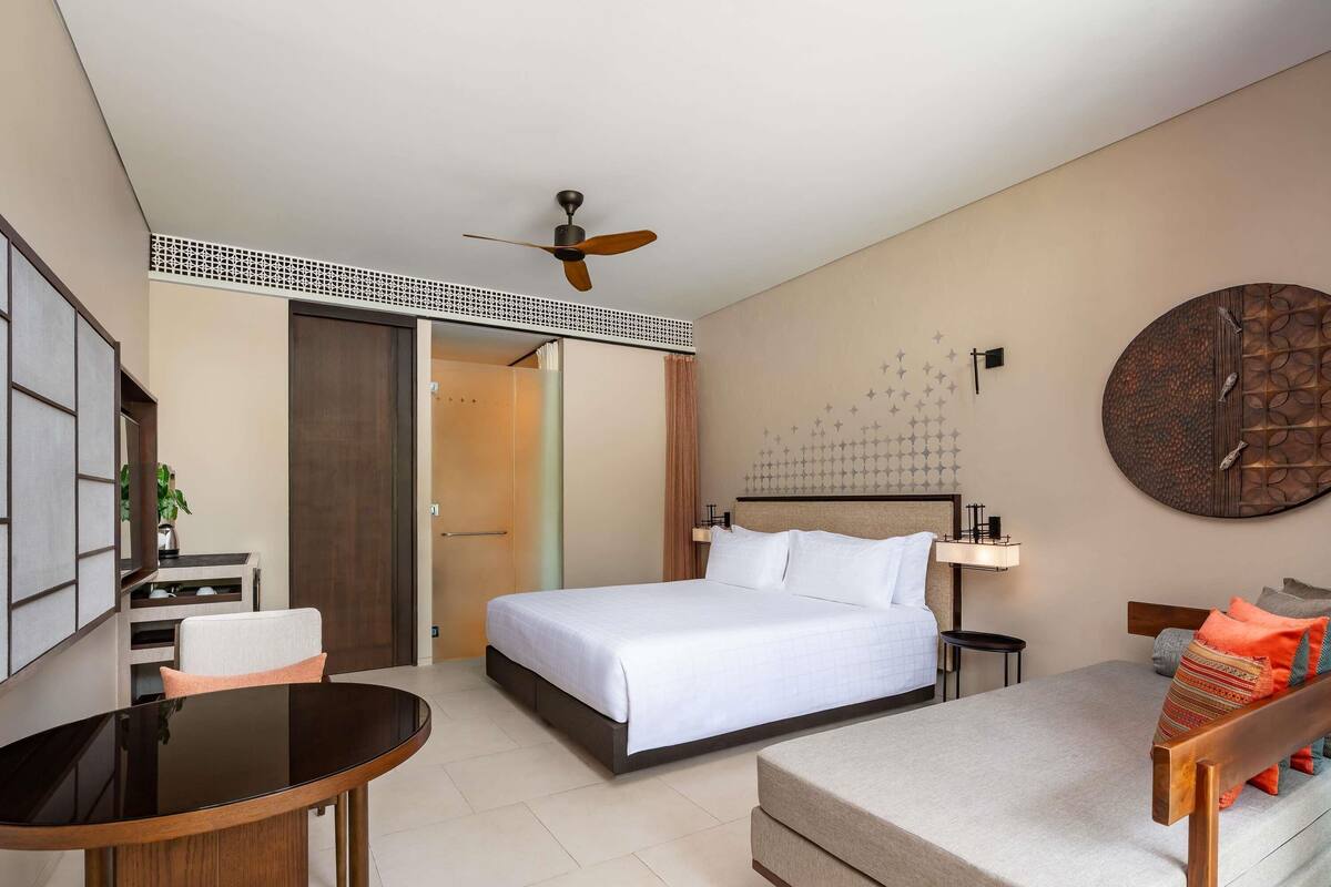 Une chambre d’hôtel équipée d’un lit, d’un bureau, d’une chaise, d’un ventilateur de plafond et d’une horloge murale.