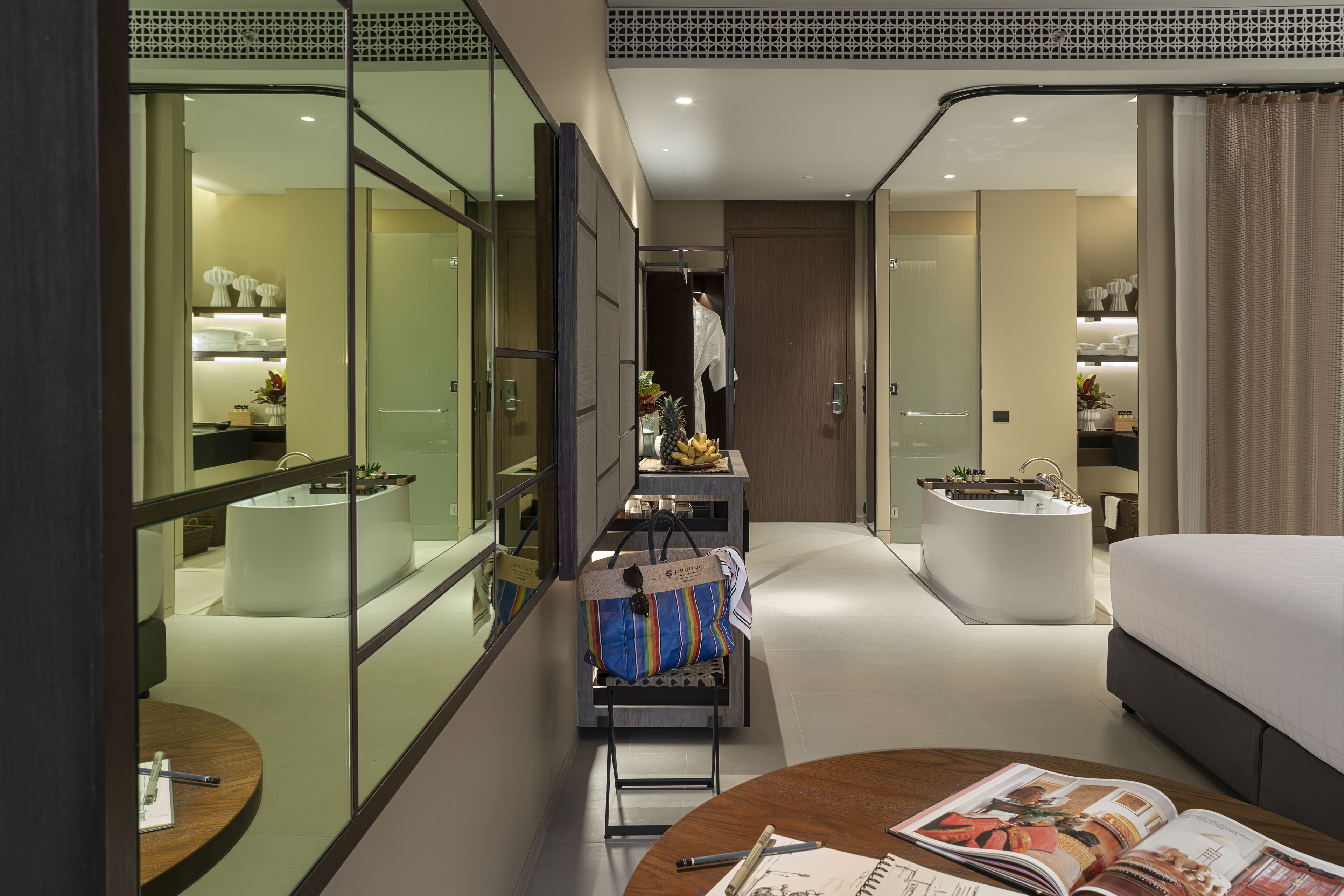A modern hotel room with a large bed, a desk with a chair, a small bathroom, and a minibar.