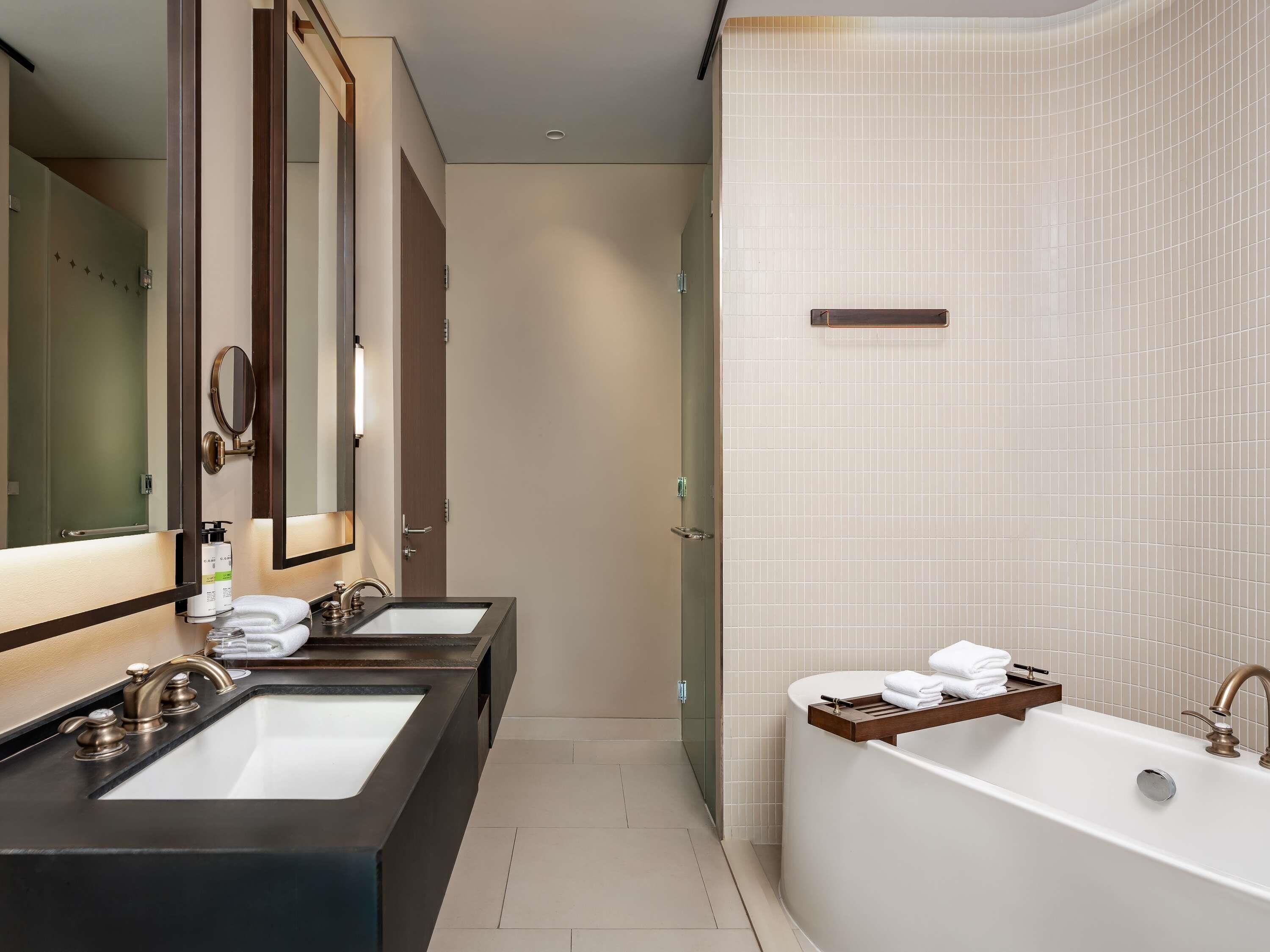 A modern bathroom with two sinks, a large bathtub, and a mirror.