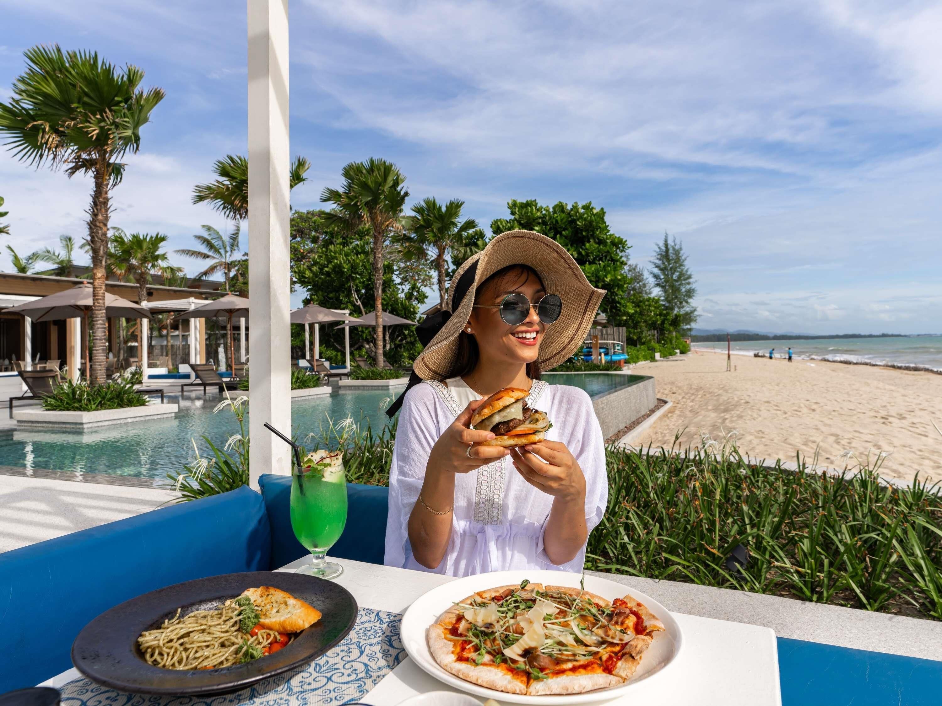 Une personne est assise à une table, avec une piscine et une plage en arrière-plan.