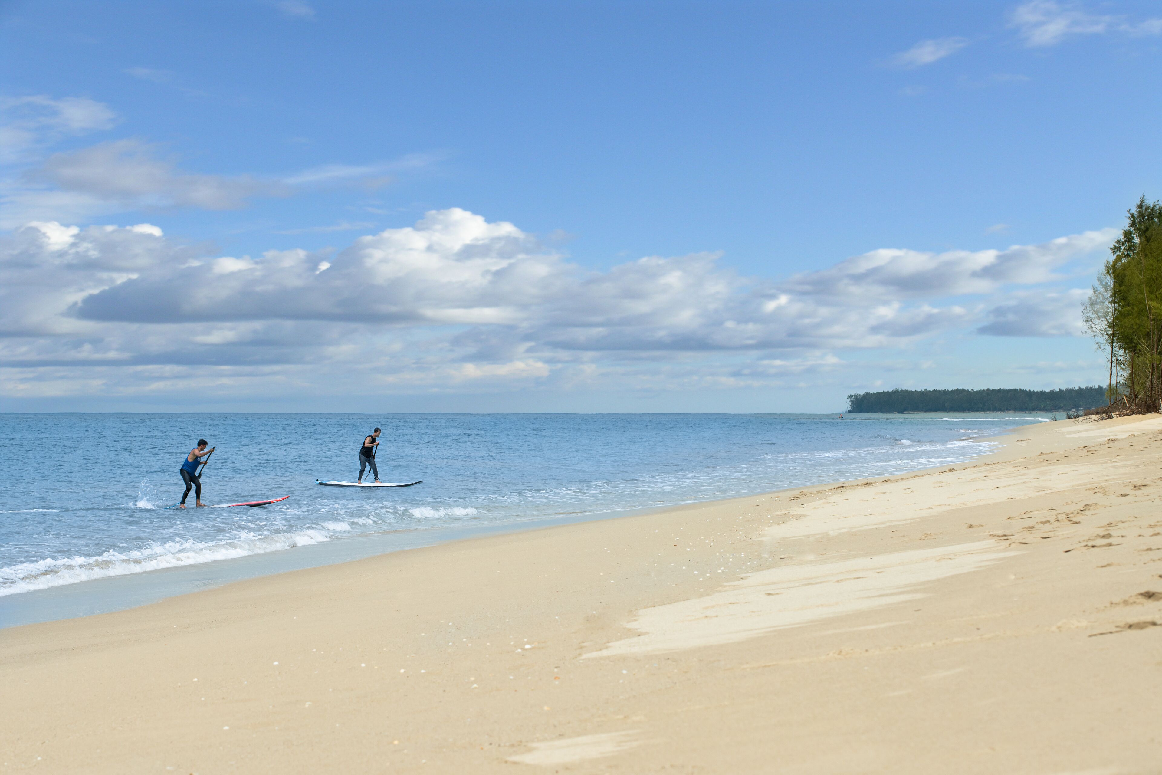 A beach with two people on surfboards, a sandy shore, and a clear sky.