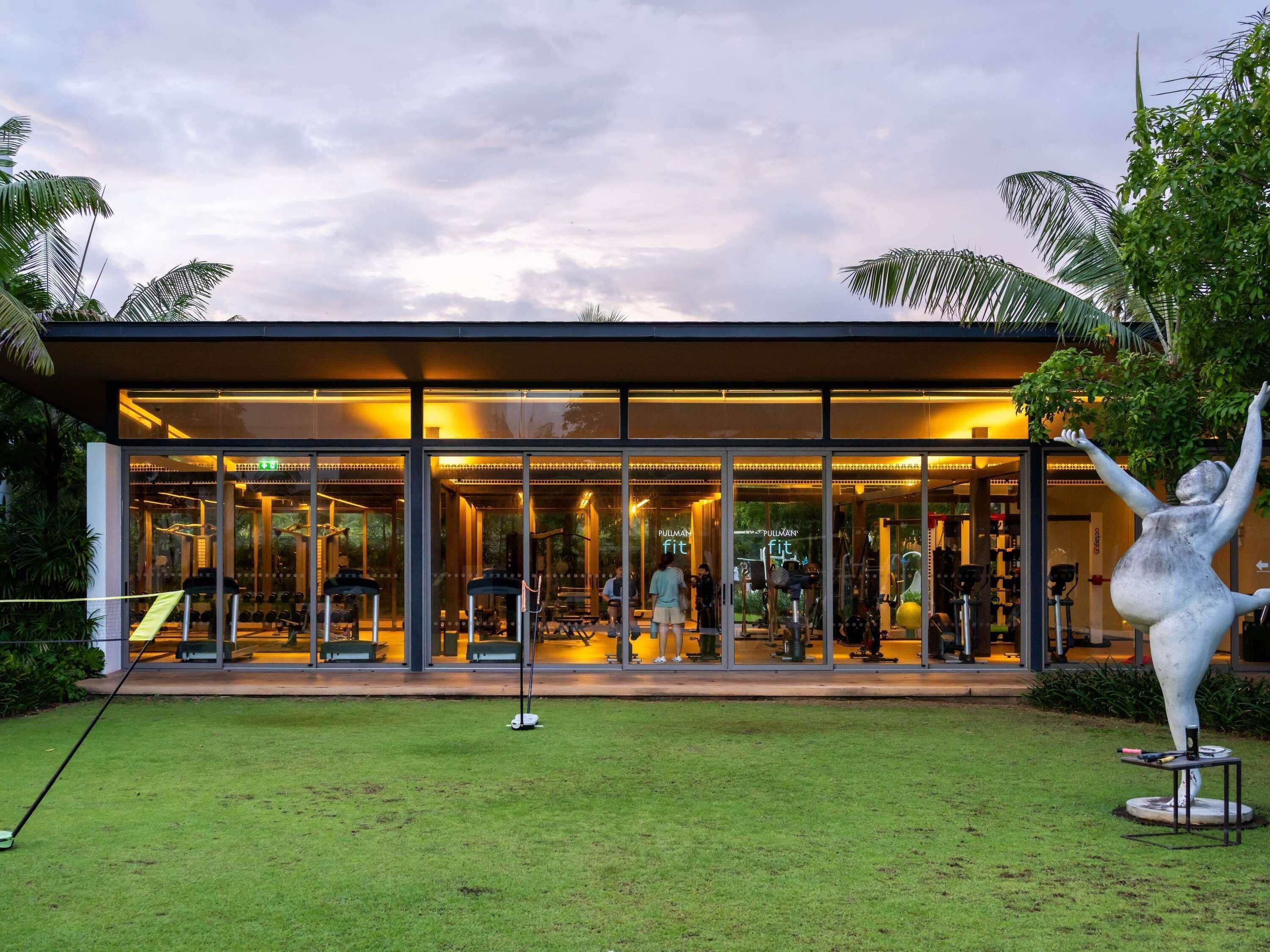 A modern fitness center with glass walls, exercise equipment, and a sculpture in the foreground.
