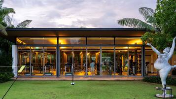 A modern fitness center with glass walls, exercise equipment, and a sculpture in the foreground.