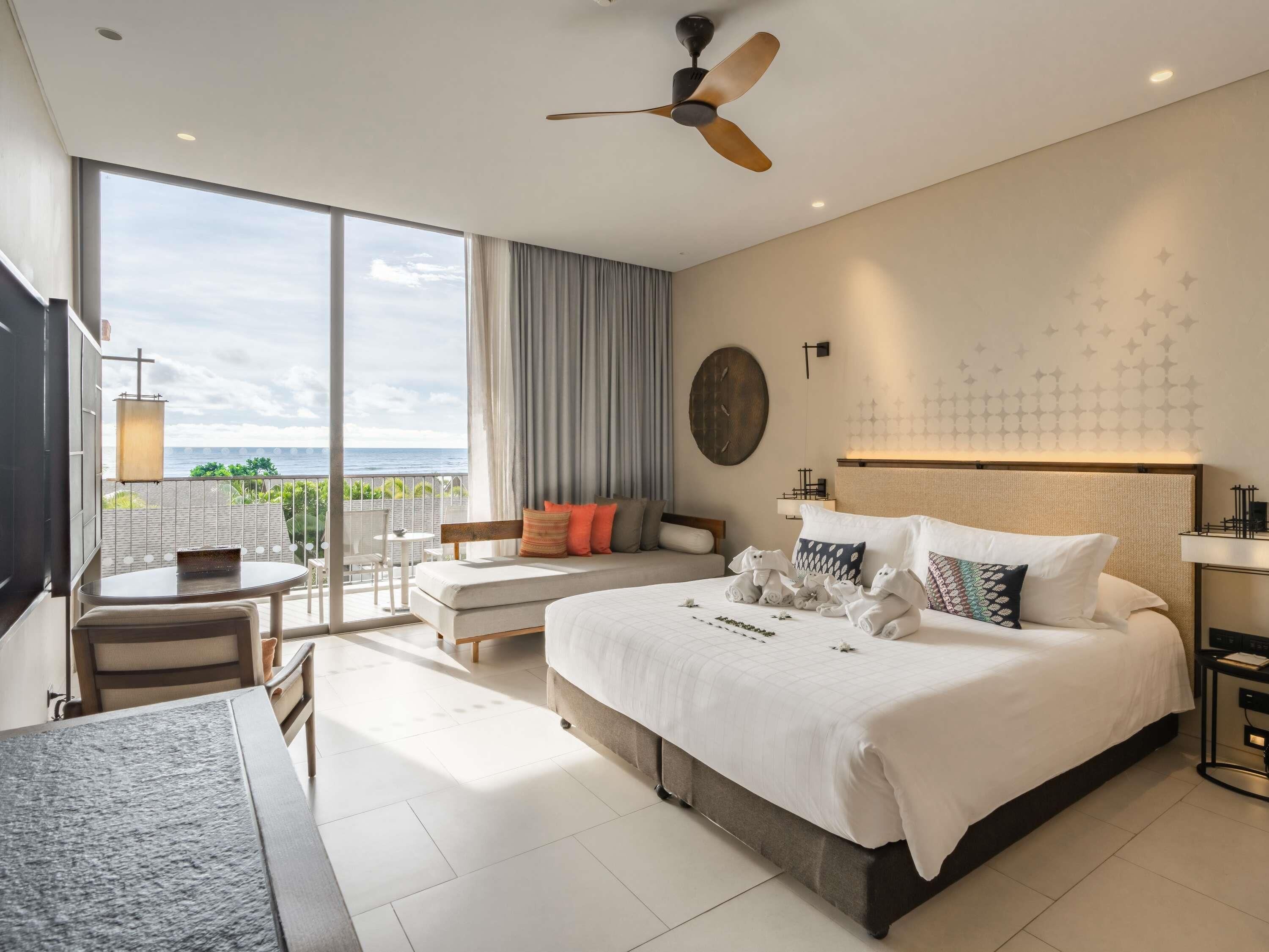 A hotel room with a large bed, a ceiling fan, a balcony with a view, and a desk with a chair.