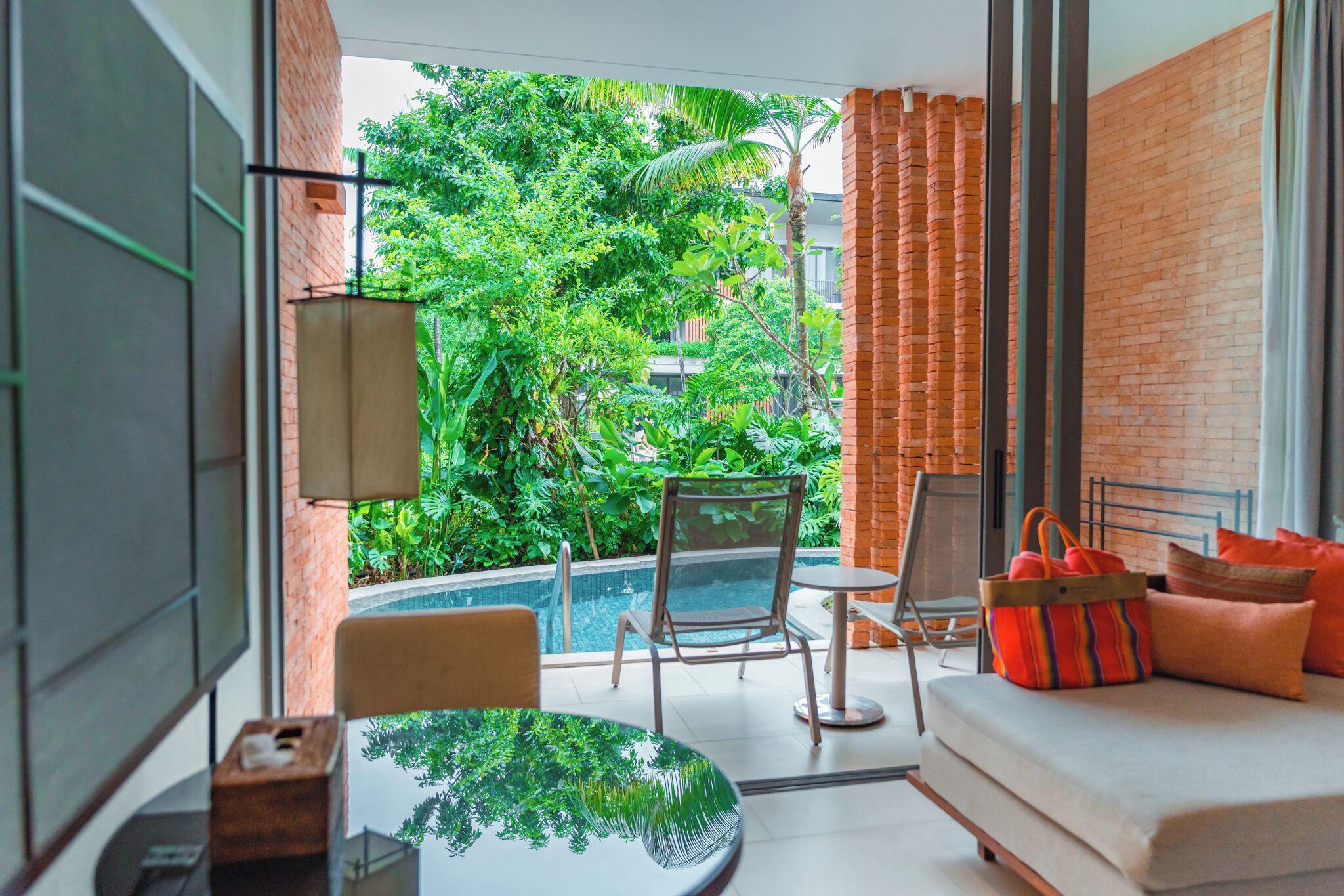 Une chambre moderne avec une porte vitrée donnant sur une piscine, un canapé avec des coussins orange et une table avec une chaise.