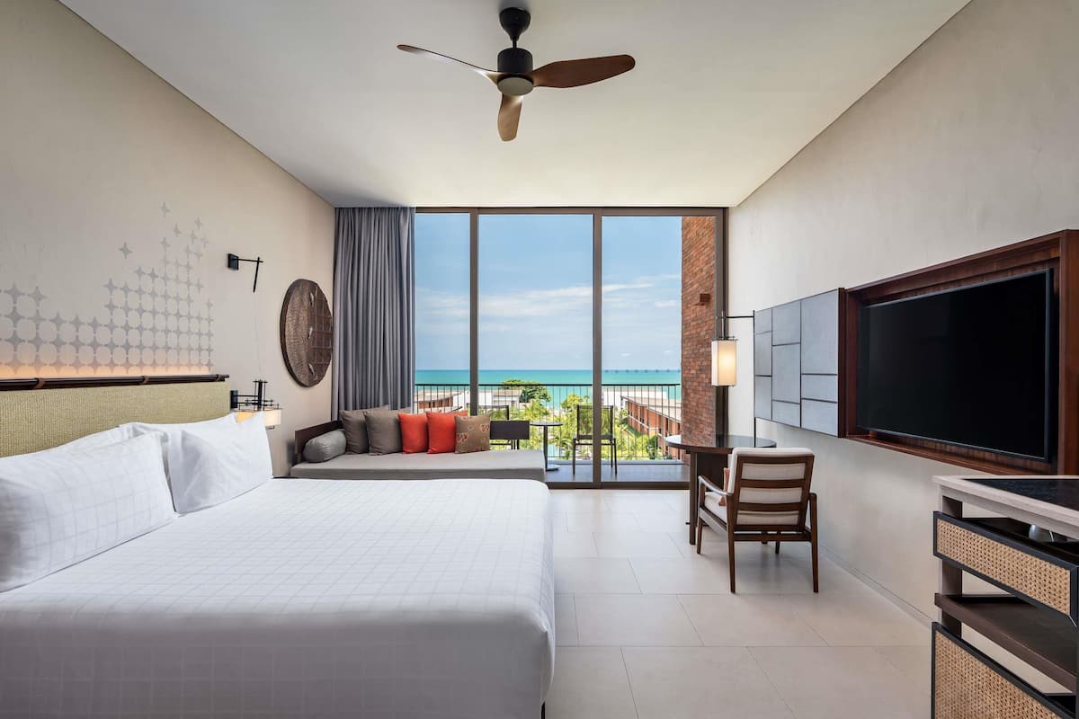 Une chambre d’hôtel équipée d’un lit, d’un bureau, d’une chaise, d’une télévision et d’un balcon avec vue sur l’océan.