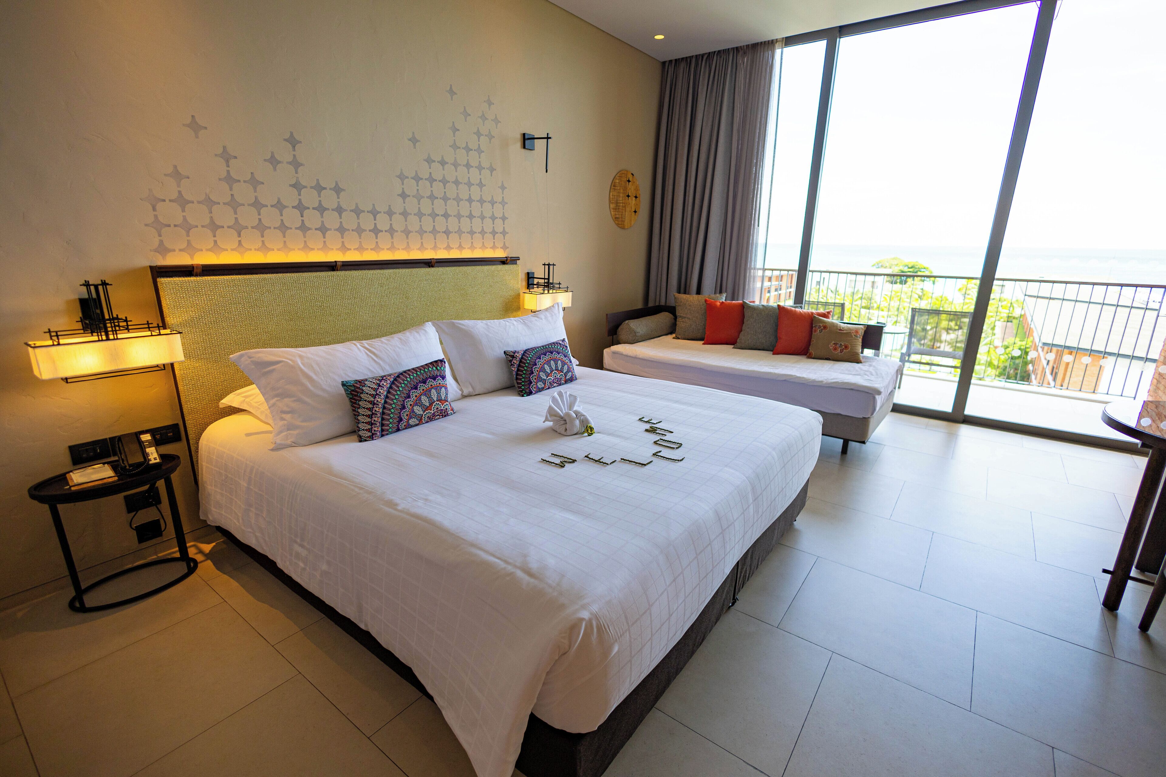 Habitación de hotel con dos camas, una mesita de noche, una lámpara, vista al exterior y un adorno en la pared.