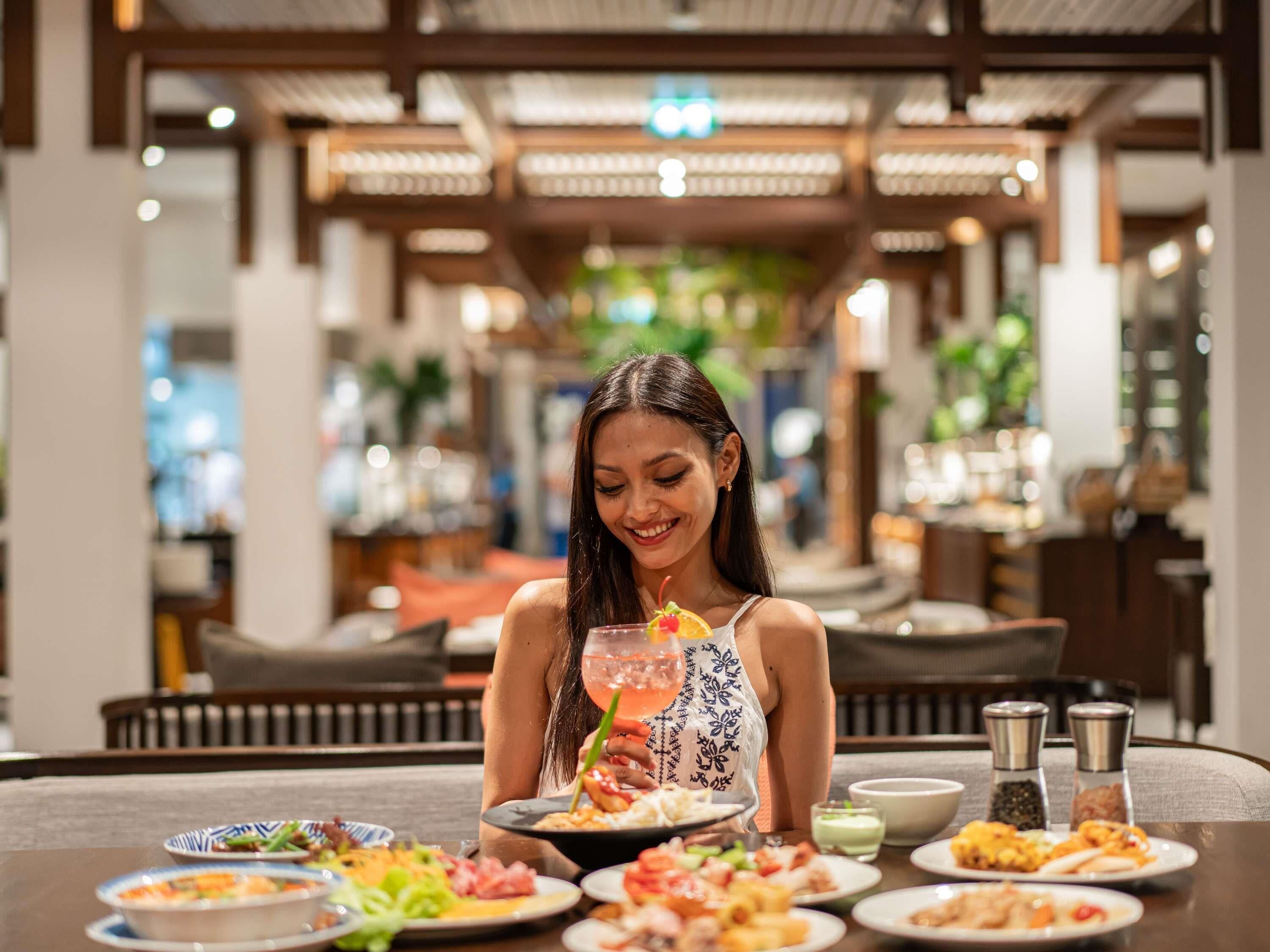 A restaurant interior with a dining table set with various dishes, a person holding a drink, and a modern interior design.