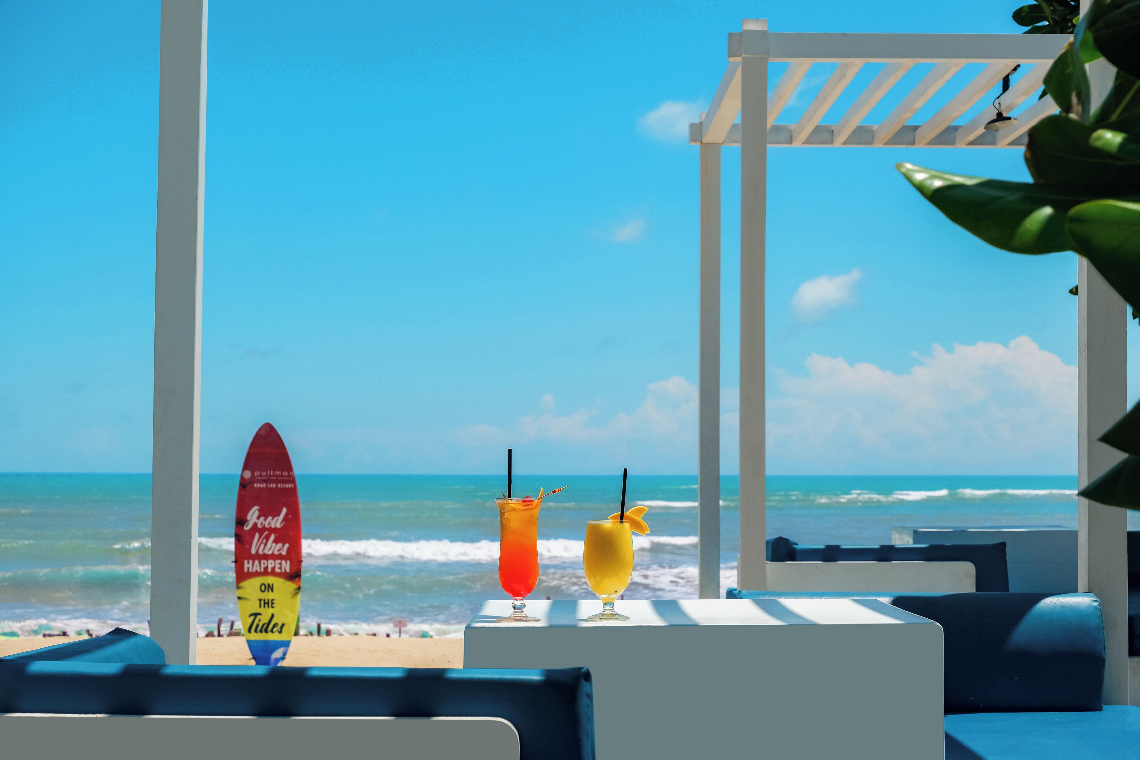 A beach view with a surfboard and two drinks on a table.
