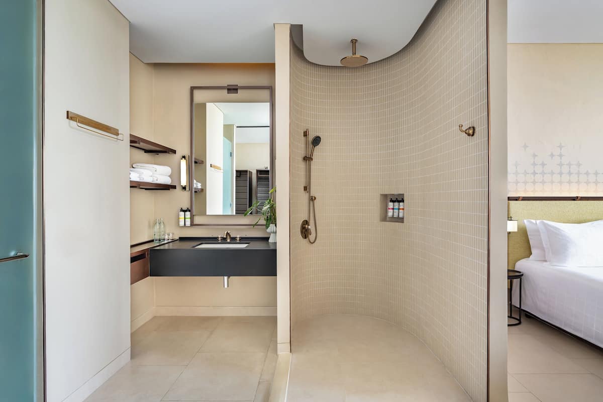Une salle de bain moderne avec douche, lavabo et un lit dans la pièce adjacente.