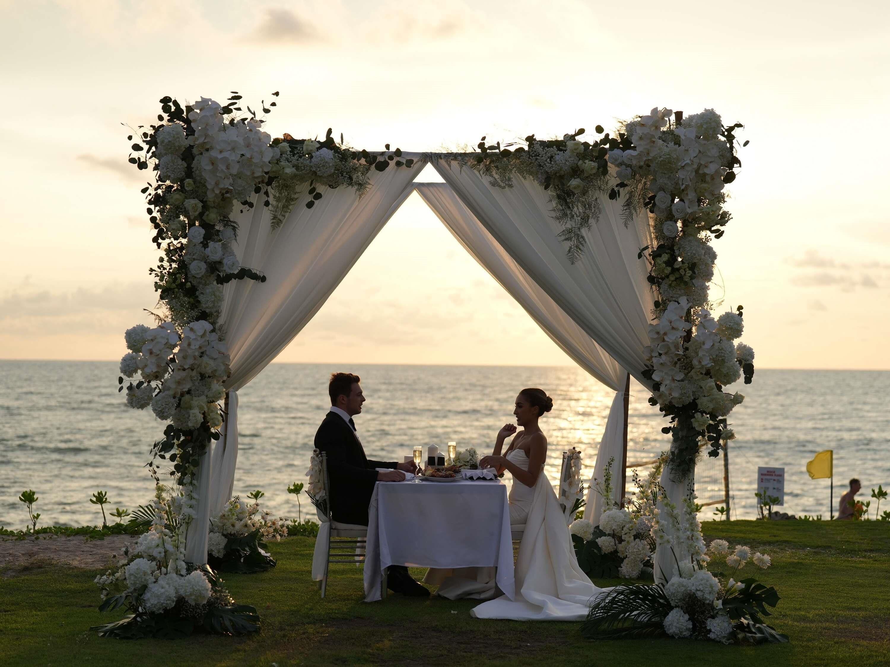 Una ceremonia de boda con un arco floral blanco y una mesa preparada para dos.