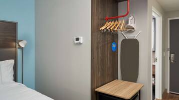 Quarto de hotel com uma cama, uma mesinha, aquecedor fixado na parede, cabideiro e uma porta que dá para um banheiro.