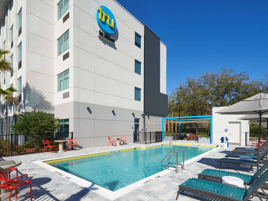A modern hotel with a swimming pool, outdoor seating, and a clear blue sky.