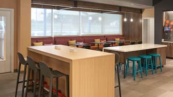 A modern cafe with wooden tables, bar stools, and a seating area with red cushions.