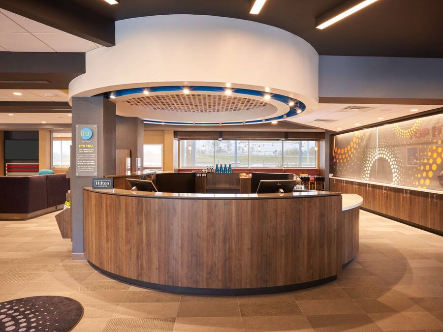 A modern hotel reception area with a curved reception desk, a seating area with a sofa and chairs, and a large window providing a view of the outdoors.