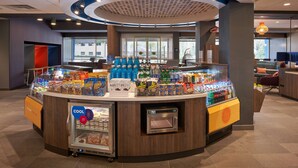 A self-service beverage station with a variety of drinks and snacks, a refrigerated display, and a coffee machine. - Tru by Hilton Jacksonville South Mandarin (Jacksonville)