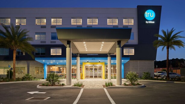 A modern hotel entrance with a covered walkway, palm trees, and a blue and white facade. - Tru by Hilton Jacksonville South Mandarin (Jacksonville)