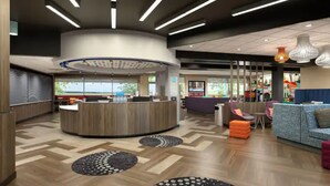 A modern lobby with a central reception desk, seating area with sofas, patterned rugs, and a view of the outdoors. - Tru by Hilton Jacksonville South Mandarin (Jacksonville)