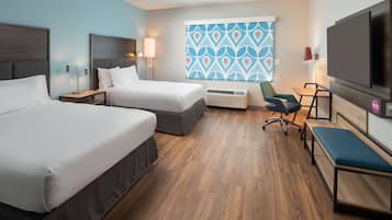 A hotel room with two beds, a desk, a chair, a TV, and a window with a geometric pattern.