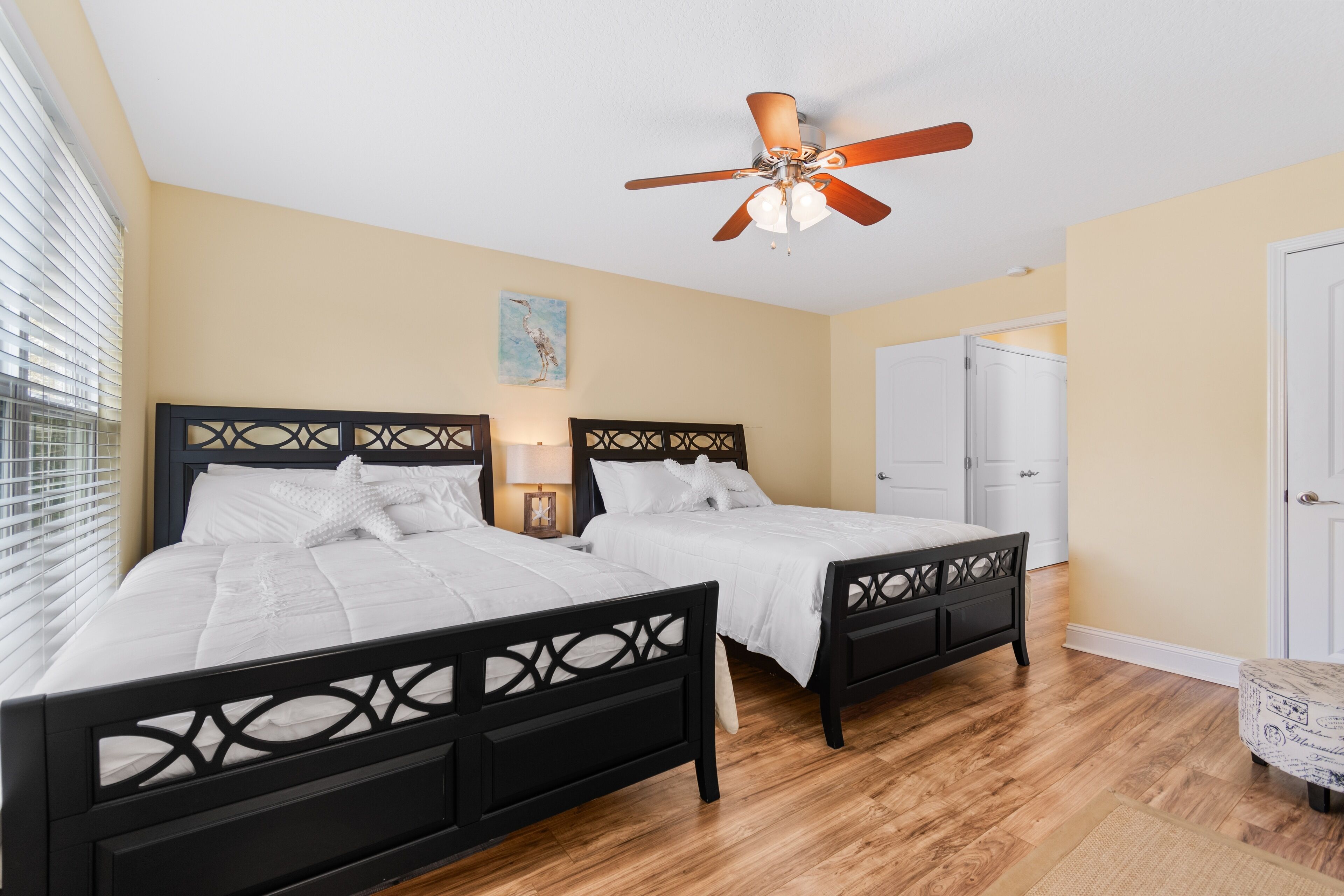 A bedroom with two beds, a ceiling fan, wooden flooring, and a door leading to another room.