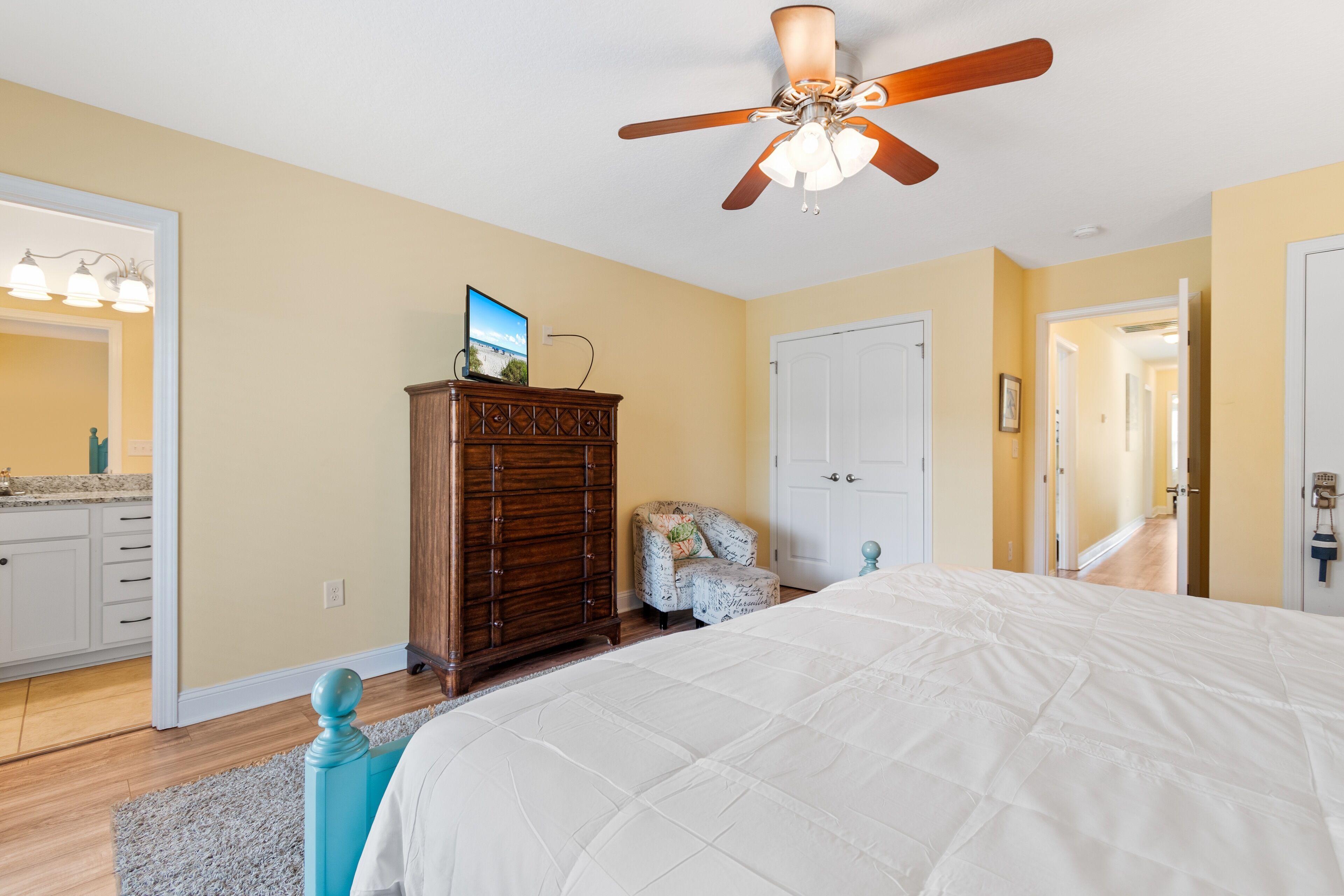 A bedroom with a bed, a dresser, a chair, and a ceiling fan.