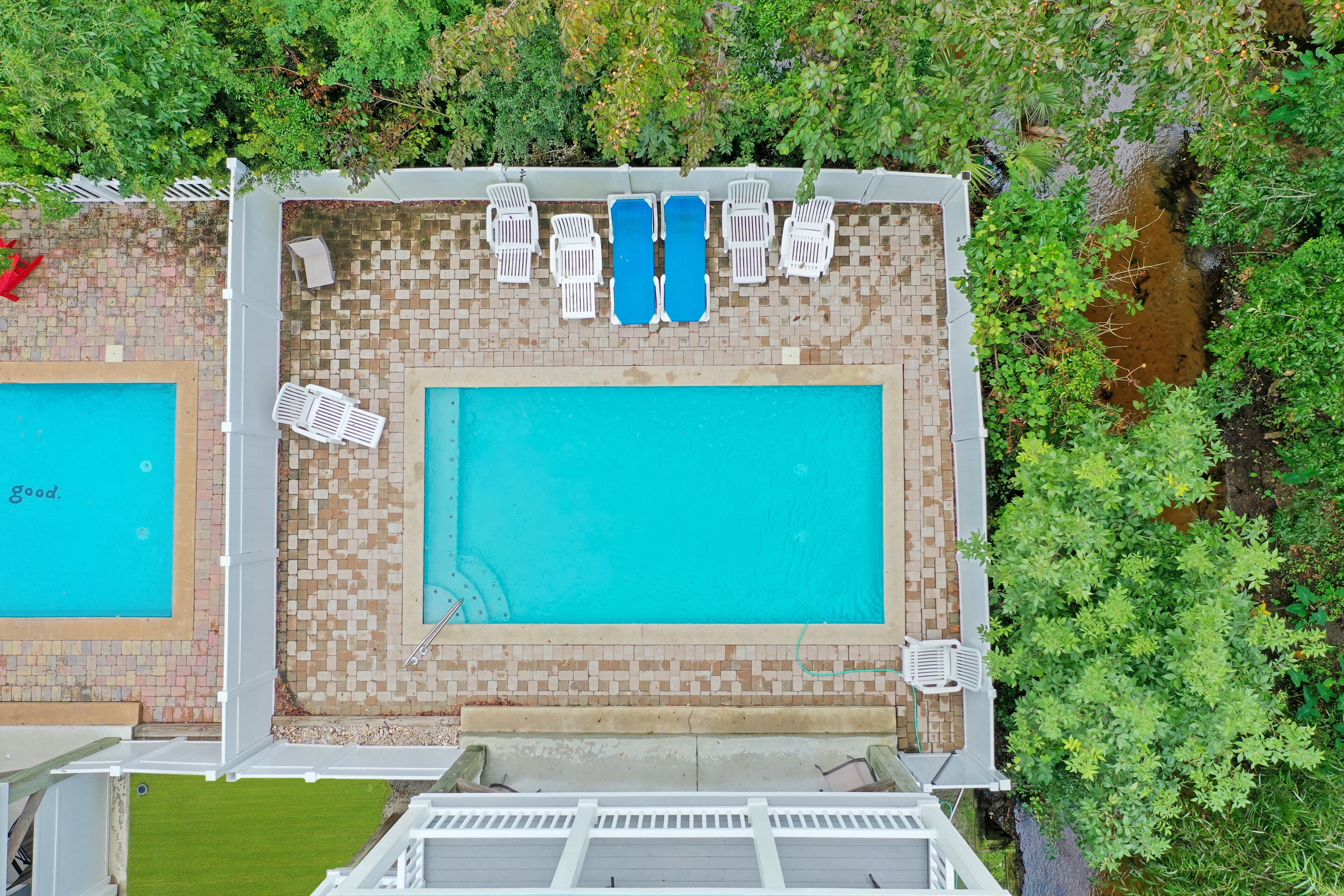 An aerial view of a rooftop swimming pool with two separate pools, surrounded by lounge chairs and a small garden area.