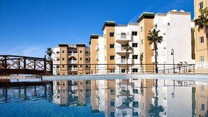 Ett hotell med en pool som speglar byggnaderna och palmerna.