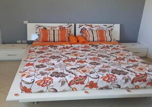 Un lit avec une couvre-lit à motifs floraux, deux oreillers, une table de chevet et une commode.