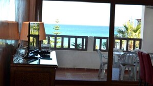Une chambre avec vue sur la mer, un bureau avec une lampe et un coin repas avec des chaises.