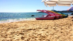 Une plage de sable où s’alignent plusieurs bateaux aux couleurs vives, un ciel bleu clair et une mer calme.