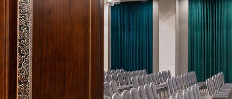 A conference room with rows of grey chairs, teal curtains, and a wooden door with intricate carvings.