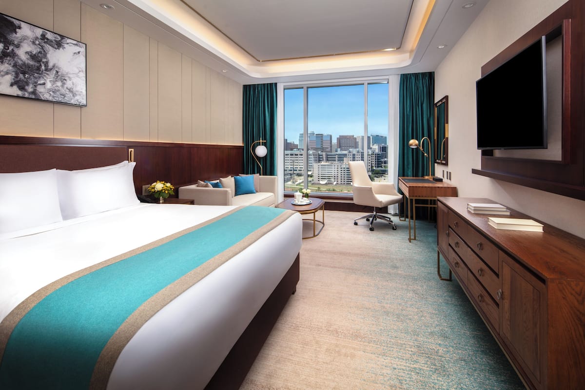A hotel room with a large bed, a desk, a chair, a TV, and a view of the city.