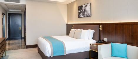 A modern hotel room with a large bed, a bedside table, a nightstand, a sofa, and a painting on the wall.