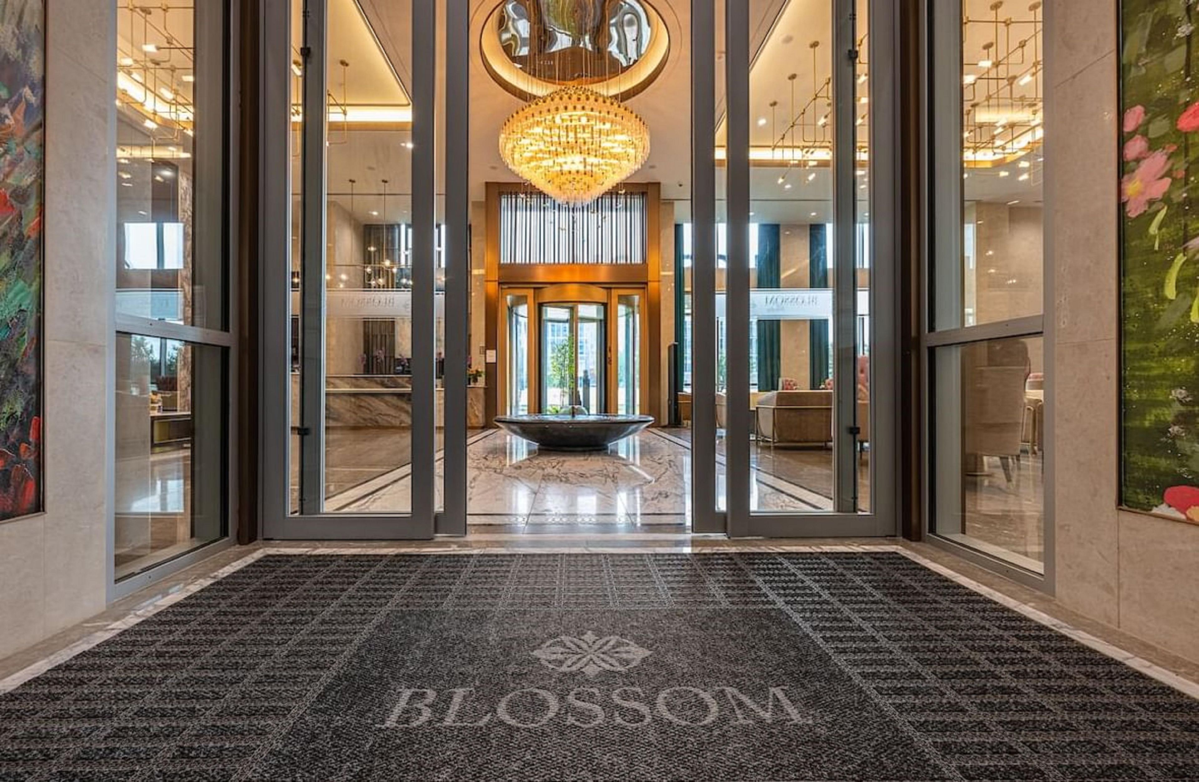 A hotel lobby with a grand chandelier, a reception desk, and a carpet with the hotel's name.