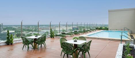 A rooftop terrace with a pool, green chairs, and a table.