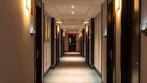 A hotel corridor with doors on both sides, a carpeted floor, and wall-mounted lighting.