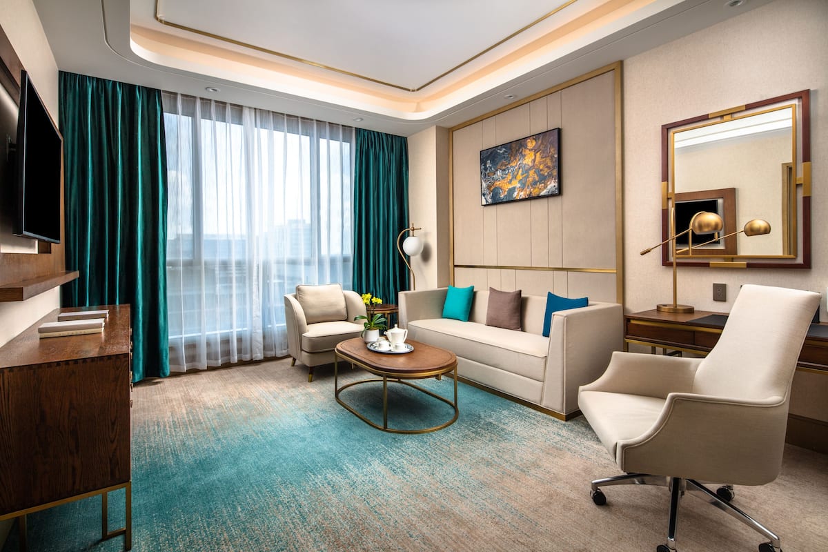 A modern hotel room with a sofa, armchair, coffee table, and a flat-screen TV.