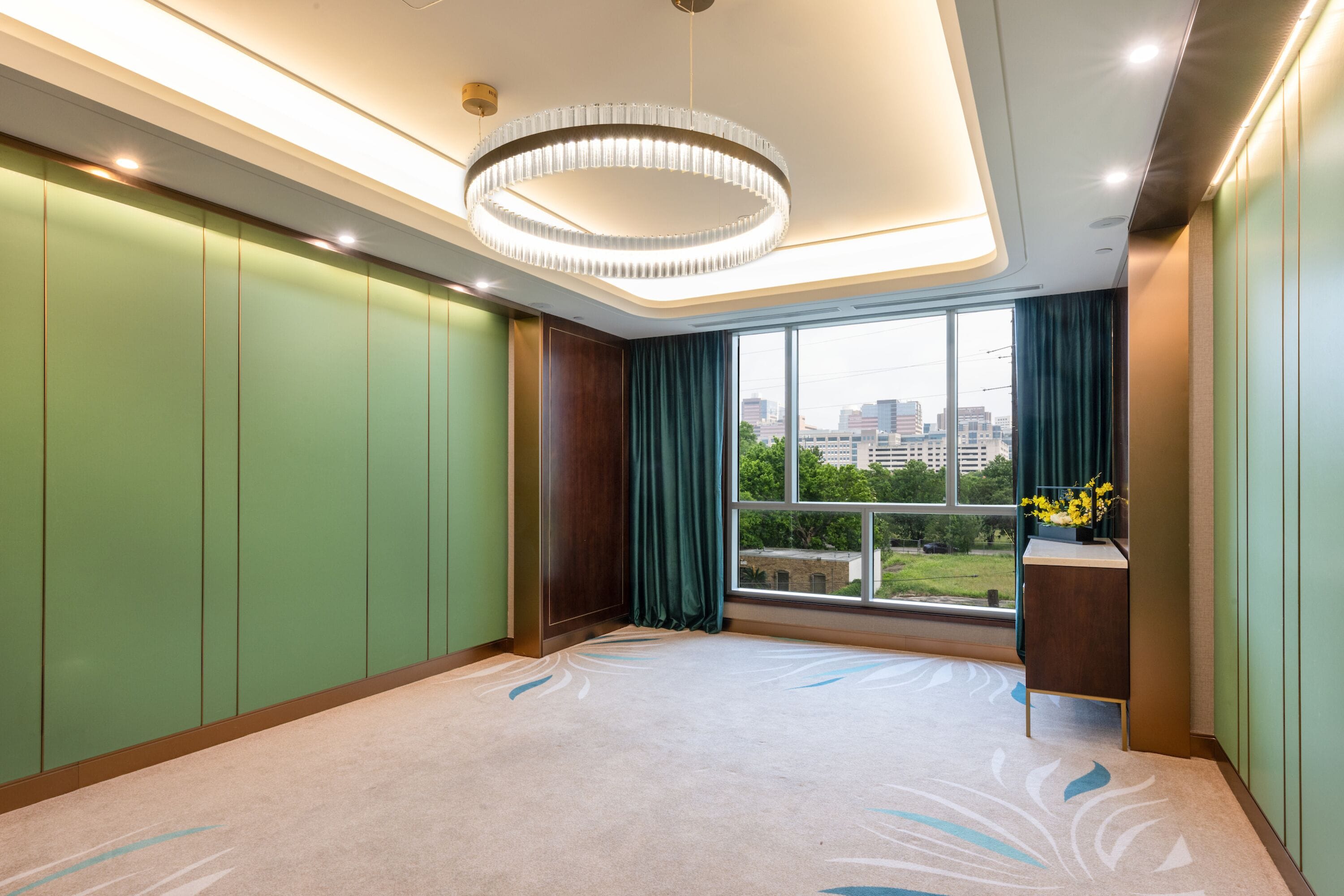 Una habitación de hotel moderna con un ventanal grande, una lámpara de araña circular y vistas a la ciudad.