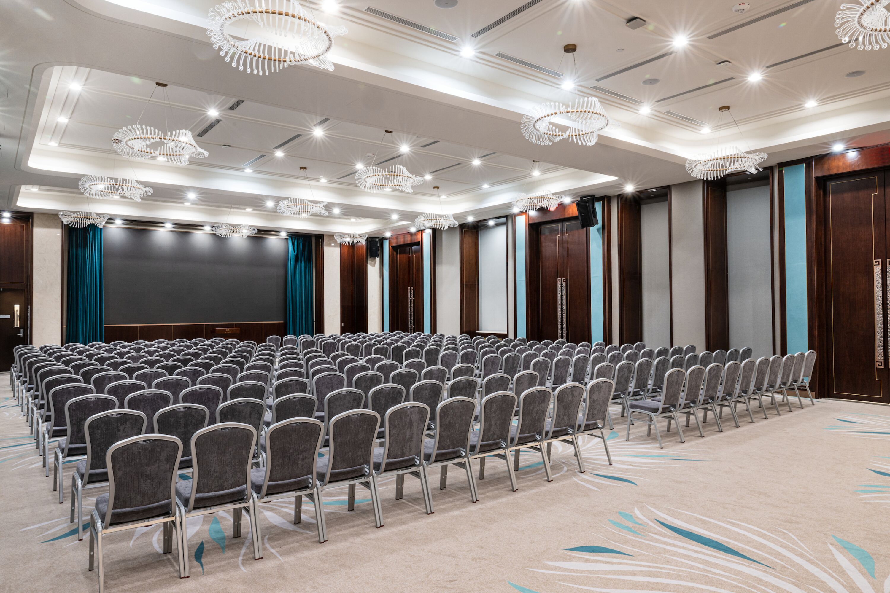 A conference room with rows of chairs, a large screen, and chandeliers.