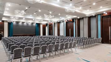A conference room with rows of chairs, a large screen, and chandeliers.