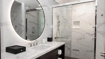 A modern bathroom with a marble vanity, a large mirror, a glass shower enclosure, and a dark wood cabinet.