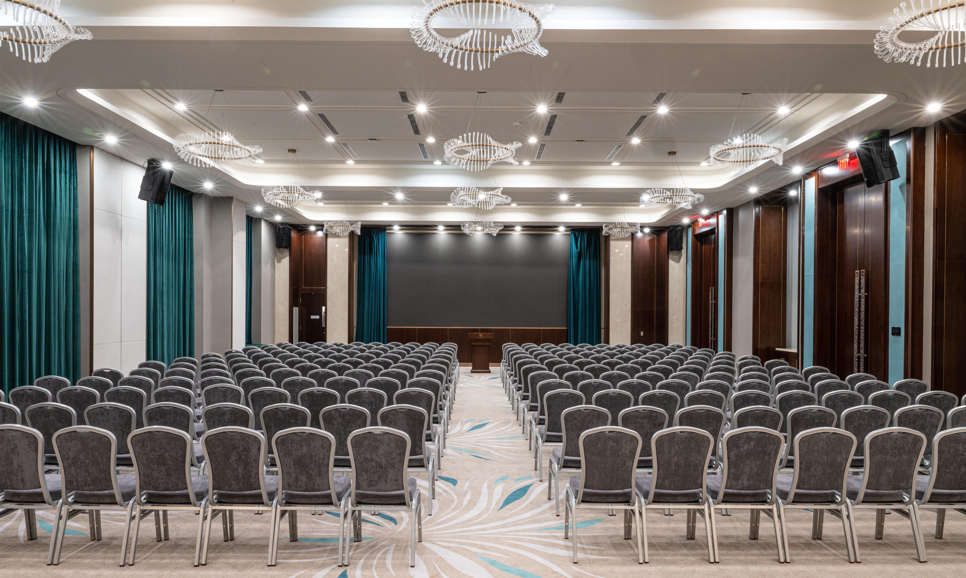 A conference room with rows of chairs, a podium, and a large screen.