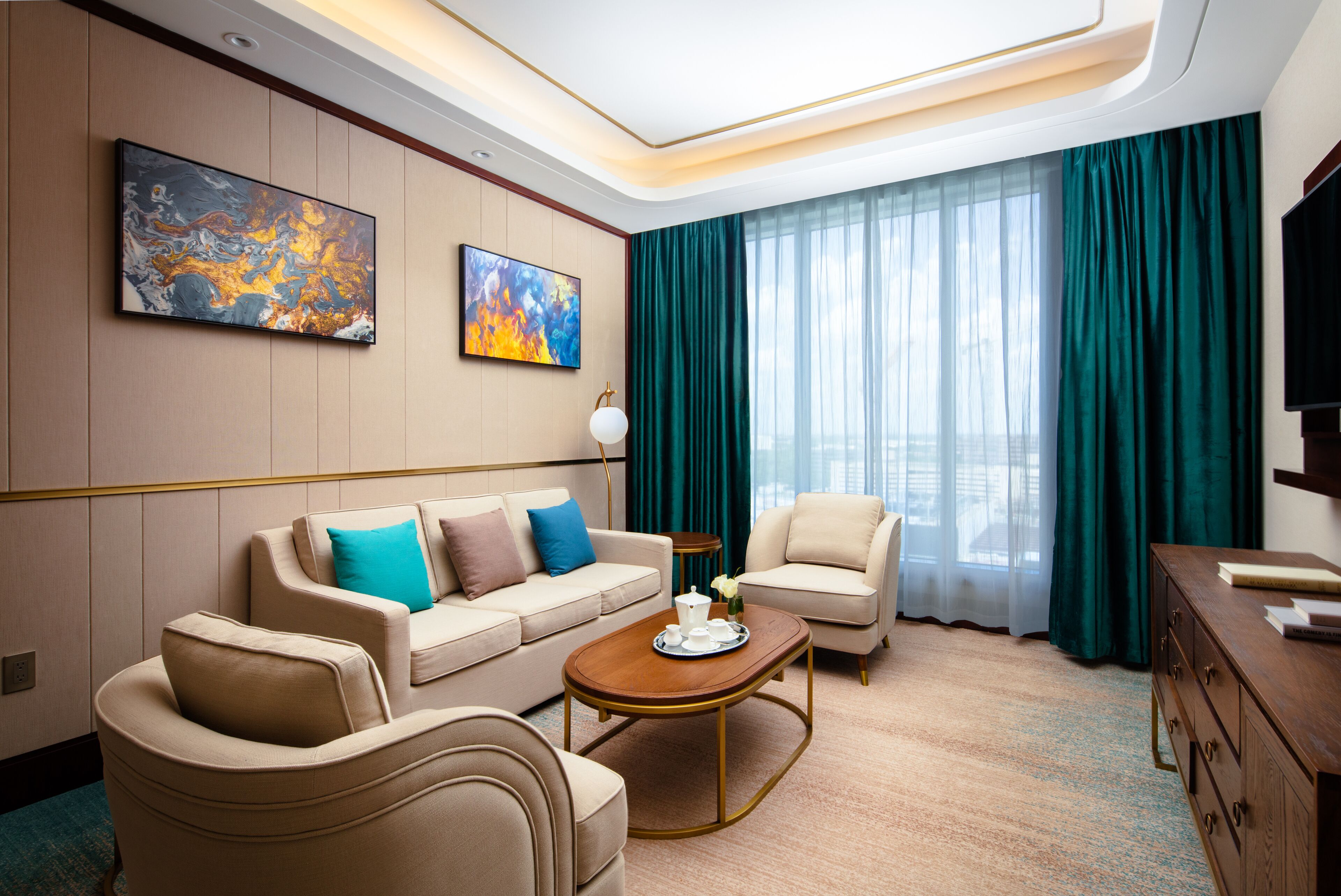 Una habitación de hotel moderna con un conjunto de sofás, una mesa de centro, un televisor y obras de arte en las paredes.
