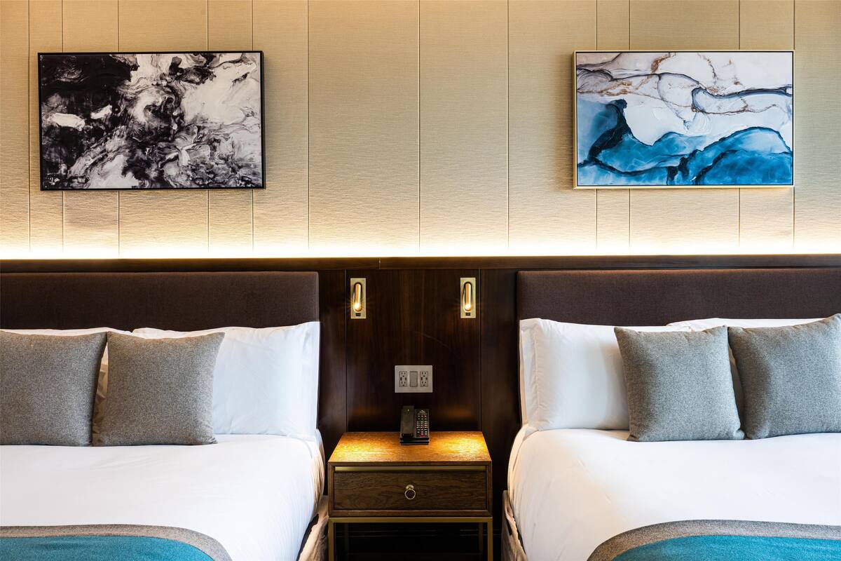 A hotel room with two beds, a nightstand with a phone, and artwork on the wall.