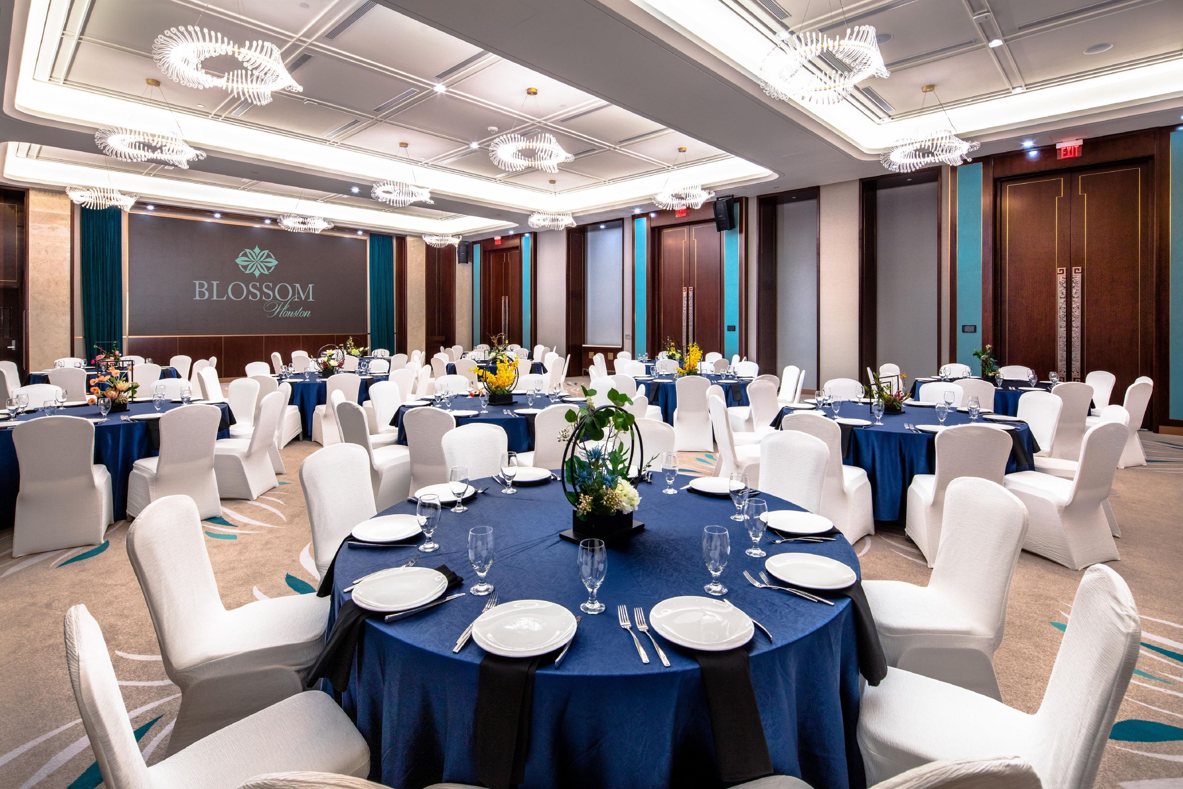 Un salón de banquetes con mesas redondas, sillas blancas y manteles azules.
