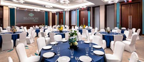 Un salón de banquetes con mesas redondas, sillas blancas y manteles azules.